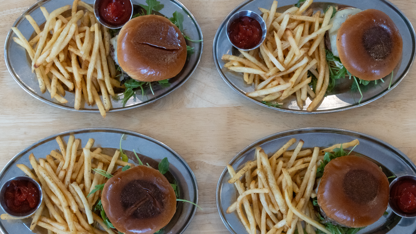 Four plates of burgers with fries and ketchup on a wooden table